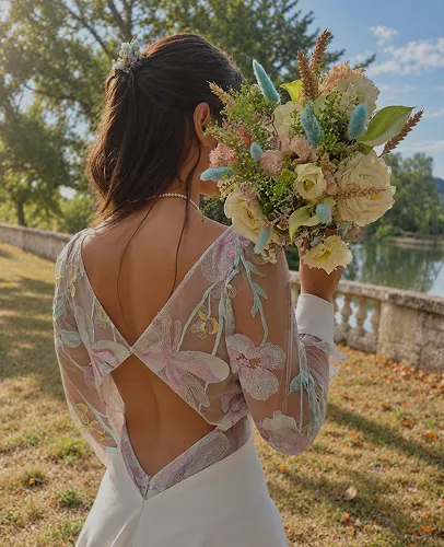 Mariée de dos en robe de dentelle, son bouquet champêtre à la main