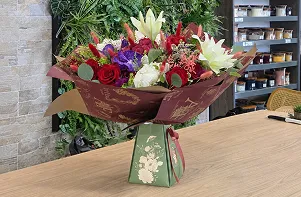 Bouquet de roses et de lys emballé, posé sur le comptoir de la boutique
