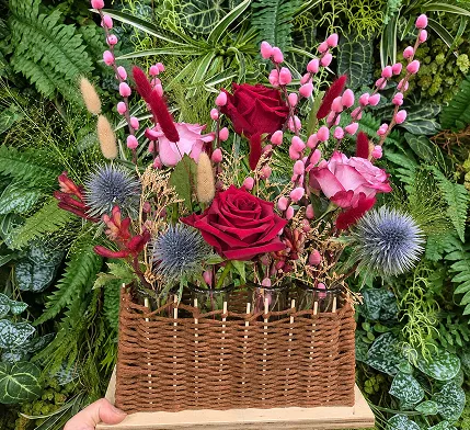 Composition de roses rouges, chardons bleus et feuillages dans un panier en osier