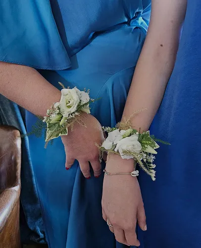 Bracelets de roses blanches et de feuillage au poignet de deux demoiselles d’honneur