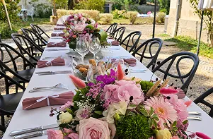 Table de réception dressée en plein air, décorée de compositions florales roses et blanches